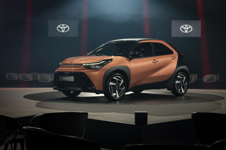 Toyota Aygo X Hybride orange sur podium, éclairée dans une mise en scène urbaine