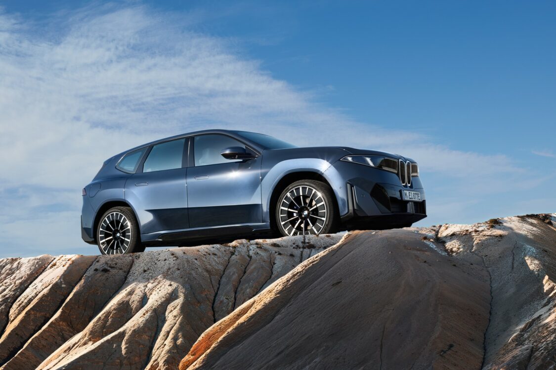 BMW iX3 vue de profil, posée sur un relief rocheux sous un ciel bleu