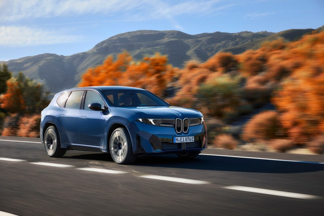 BMW iX3 en mouvement sur une route bordée de collines et de végétation automnale