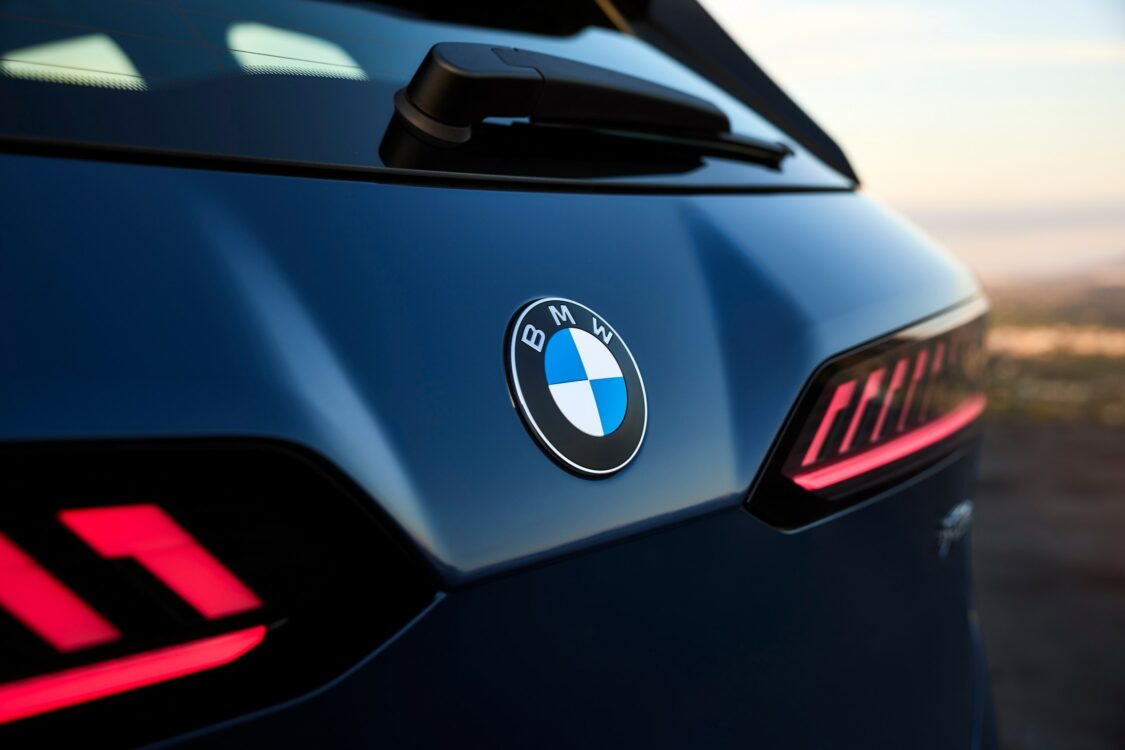 Gros plan sur le hayon arrière de la BMW iX3, logo BMW centré, avec les feux arrière LED rouges allumés.