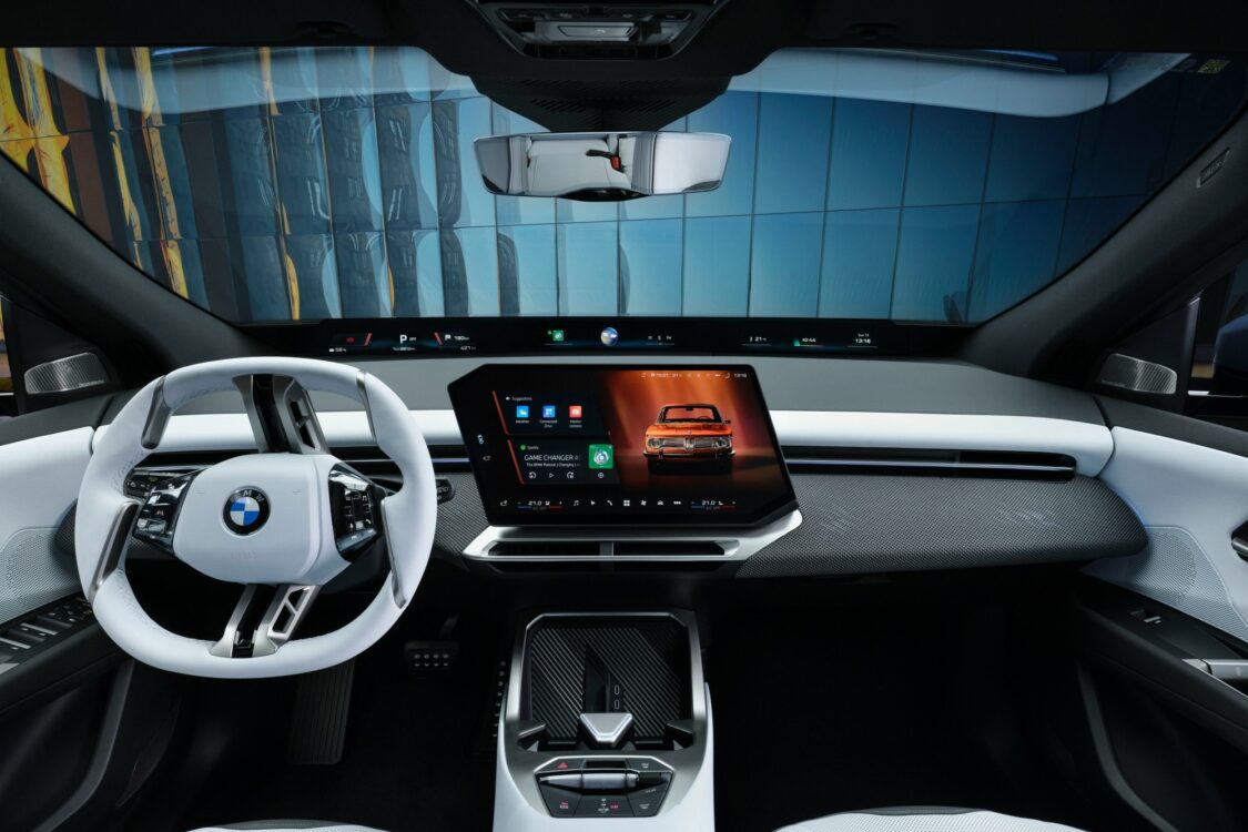 Intérieur BMW iX3, volant blanc à méplat et grand écran central numérique affichant l’interface multimédia