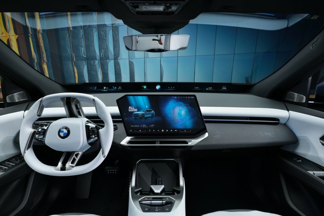 Intérieur BMW iX3, tableau de bord avec volant blanc et écran central numérique affichant l’interface multimédia et un globe stylisé