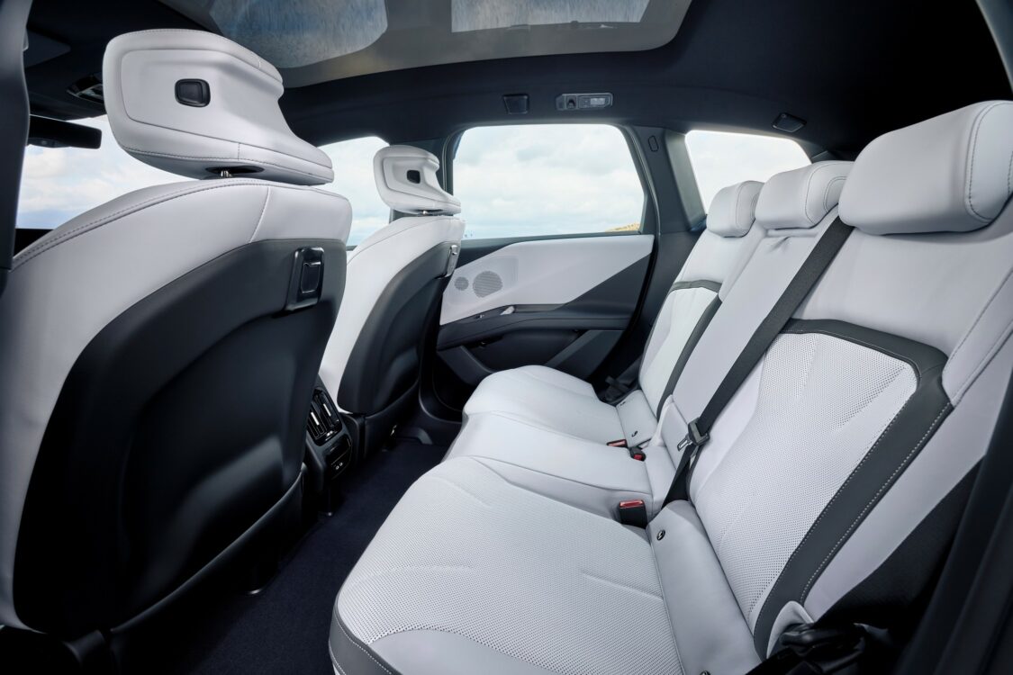 Banquette arrière de la BMW iX3 avec sellerie claire, trois appuie-têtes et ciel de toit panoramique vitré.