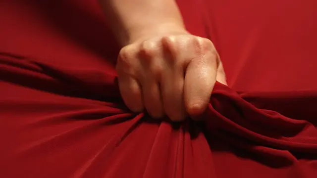 Main crispée sur un drap rouge, symbole de tension sexuelle et de plaisir physique