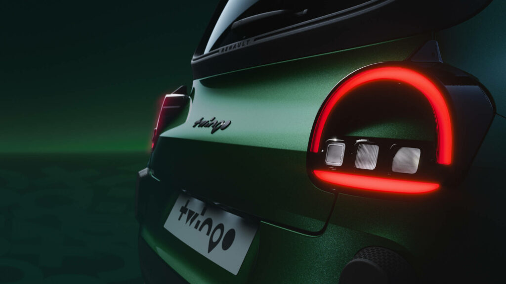 Vue arrière semi-plongée de la Twingo E-Tech electric, feux allumés, cadrage sombre et tendu.